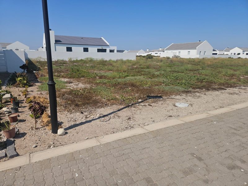 A vacant residential plot situated in a developed estate, featuring level ground and street-side access.