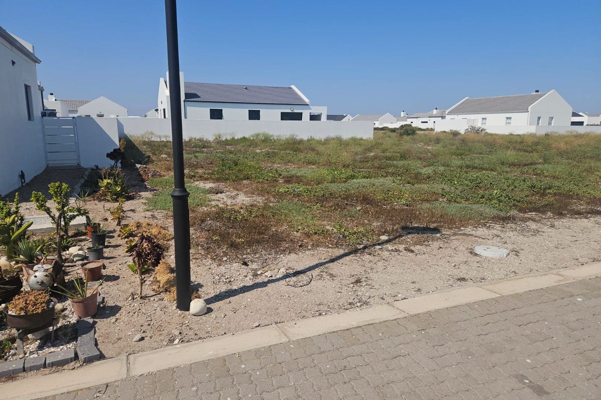 A vacant residential plot situated in a developed estate, featuring boundary walls and street-level access.