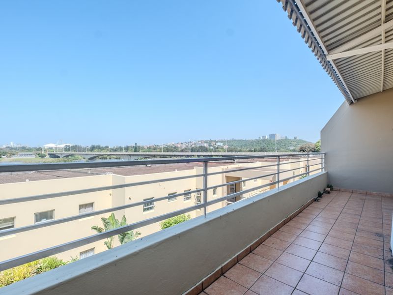 A spacious balcony featuring tiled flooring, a metal balustrade, and a retractable awning, offering elevated views of the surrounding area.