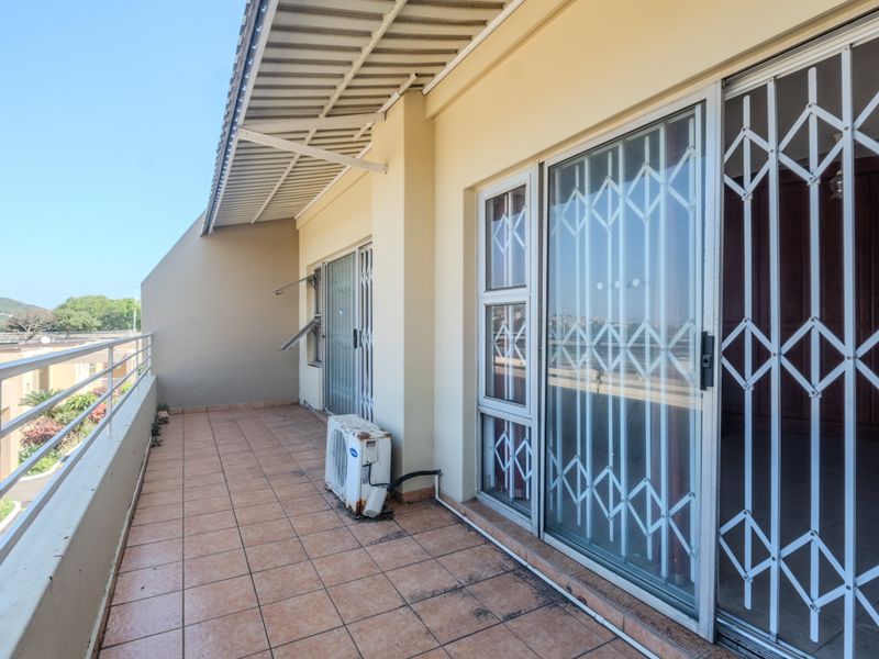 Spacious balcony featuring tiled flooring, metal security gates, and a covered roof area, offering an outdoor space accessible through sliding glass doors.