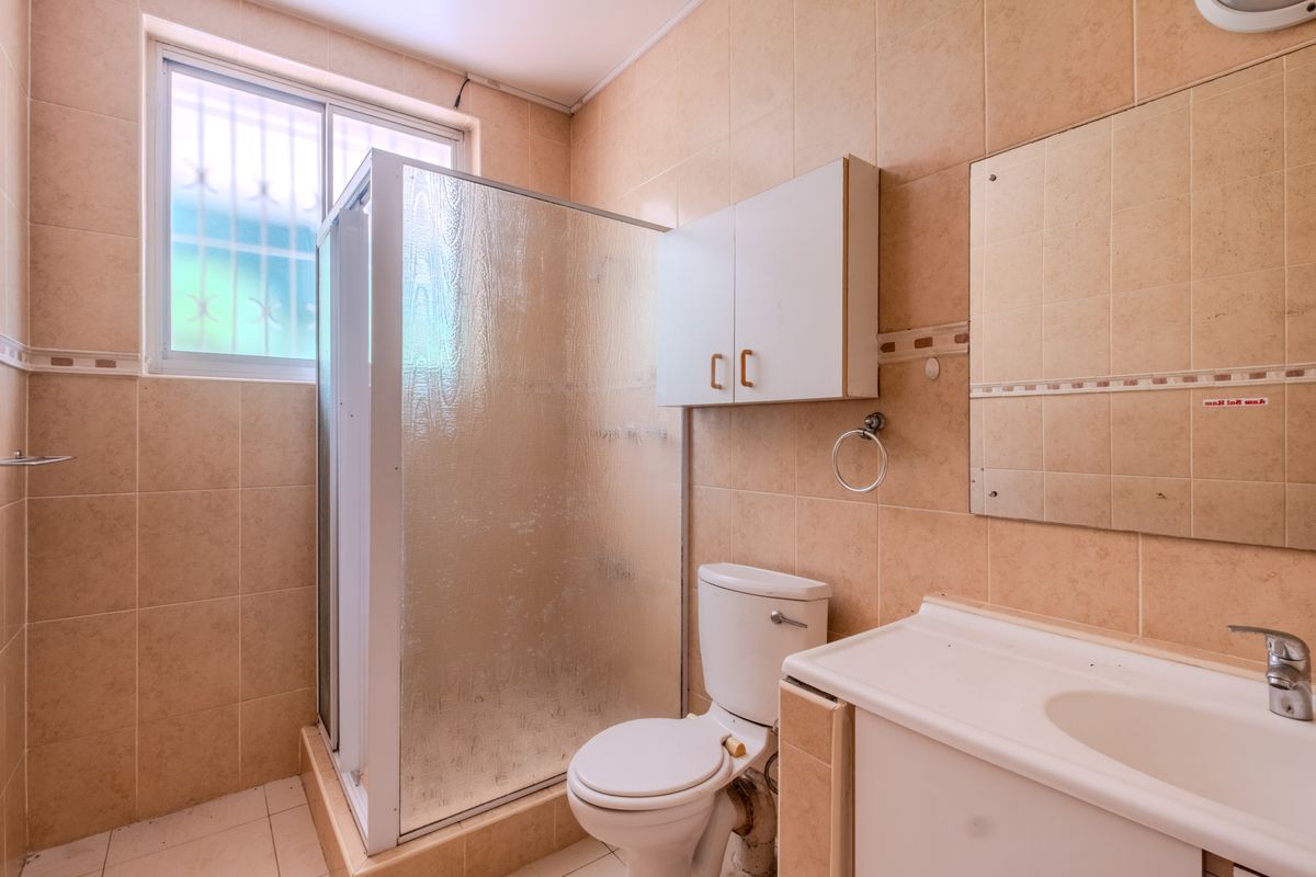 A functional bathroom featuring a shower enclosure, toilet, vanity basin, and wall-mounted storage cabinet, finished with neutral-toned wall and floor tiles.