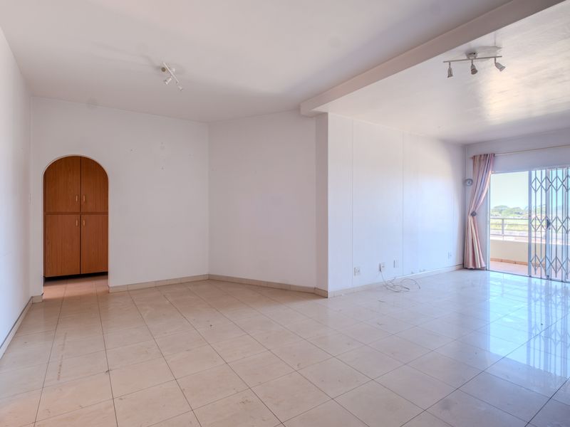 Spacious, empty living area featuring tiled flooring, a built-in arched storage cupboard, and sliding door access to an outdoor balcony.