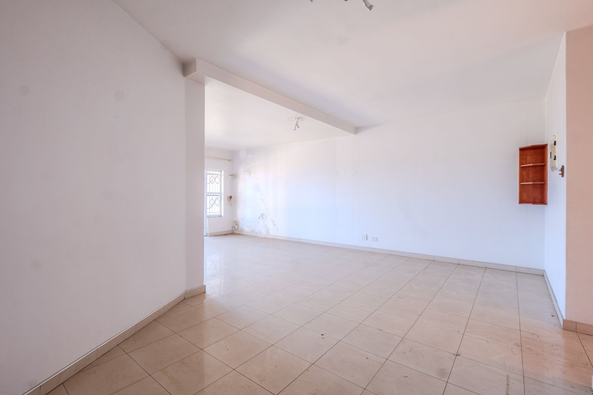 An empty, open-plan living area featuring tiled flooring and built-in wall shelving, requiring cosmetic attention to the walls.