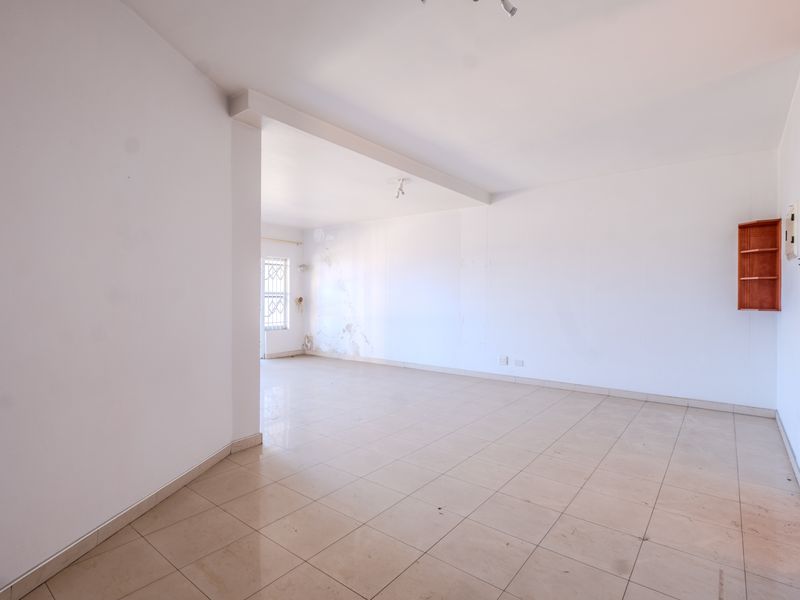 An empty, open-plan living area featuring tiled flooring and built-in wall shelving, requiring cosmetic attention to the walls.