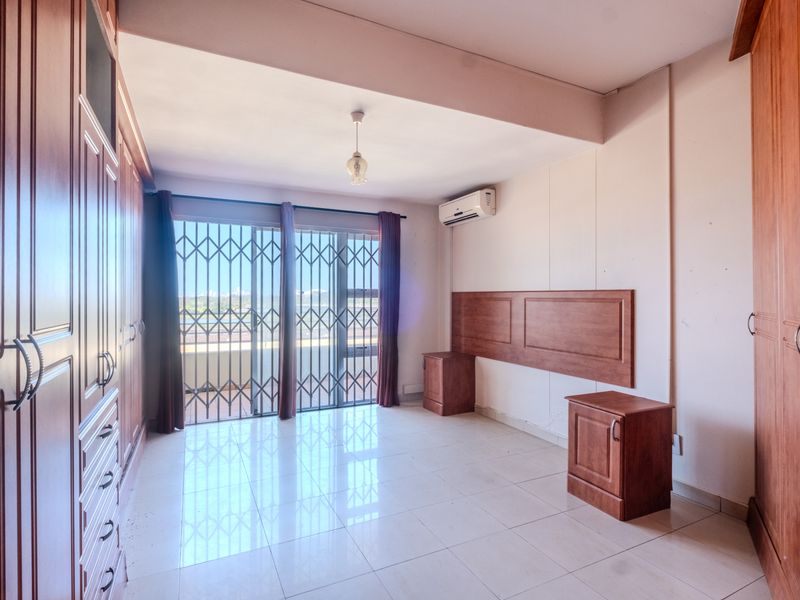 Spacious bedroom featuring extensive built-in cabinetry, tiled flooring, air conditioning, and a sliding door leading to a balcony with security gate.