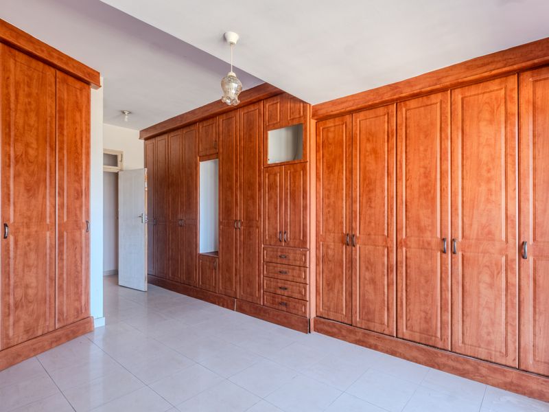 A spacious bedroom featuring extensive built-in wooden cabinetry and wardrobes with tiled flooring throughout.
