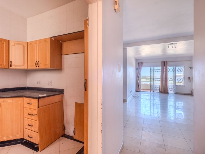 Open plan apartment layout featuring a kitchen with wooden cabinetry and a spacious living area leading to a balcony with security gates.