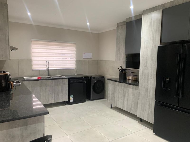 Modern kitchen featuring contemporary grey-toned cabinetry, stone countertops, tiled backsplash, and integrated space for laundry appliances.