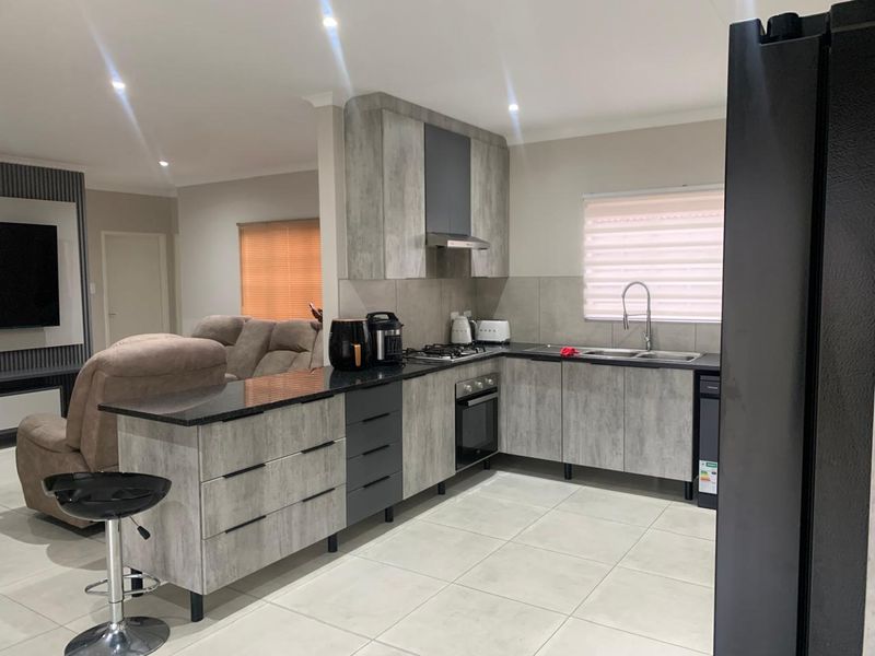 Modern open-plan kitchen featuring grey textured cabinetry, granite countertops, gas hob, and integrated oven, seamlessly flowing into the adjacent living area.