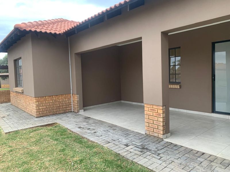 A covered patio area featuring tiled flooring, brick accents, and direct access to the garden via a paved walkway.