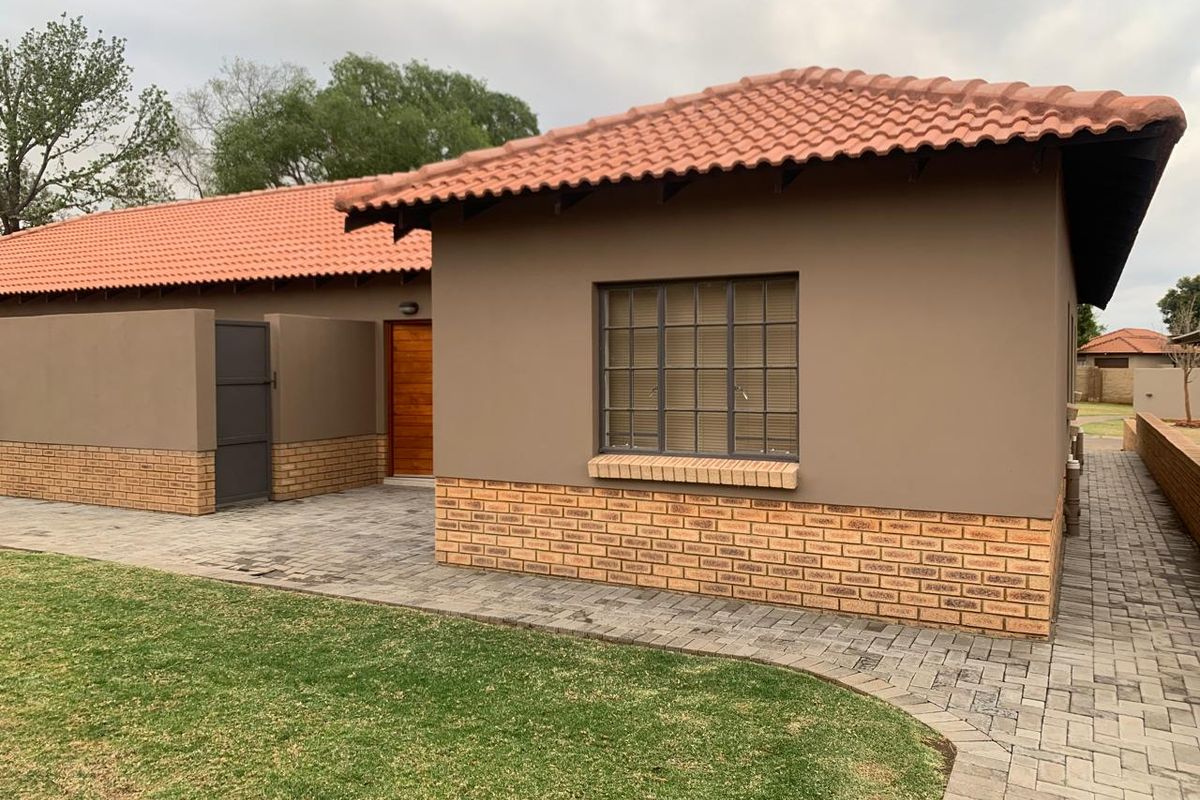A well-maintained townhouse exterior featuring a terracotta tiled roof, brick accents, and a paved walkway leading to a timber entrance door.