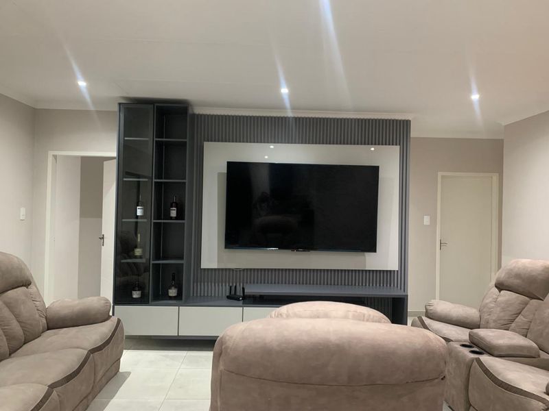 A modern living room featuring a custom built-in media unit with fluted wall paneling, recessed downlighting, and neutral tiled flooring.