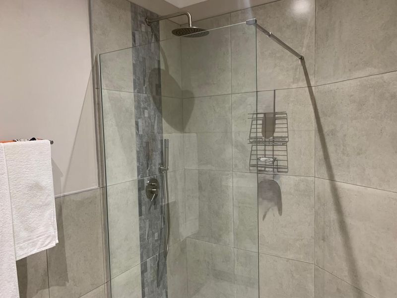A modern walk-in shower featuring large format grey tiles, a mosaic accent strip, and a contemporary rain shower head with a glass screen.