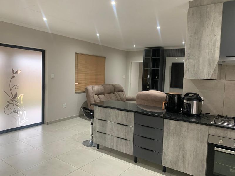 Modern open-plan kitchen and living area featuring a central island with granite countertops, built-in oven, gas hob, and contemporary cabinetry.