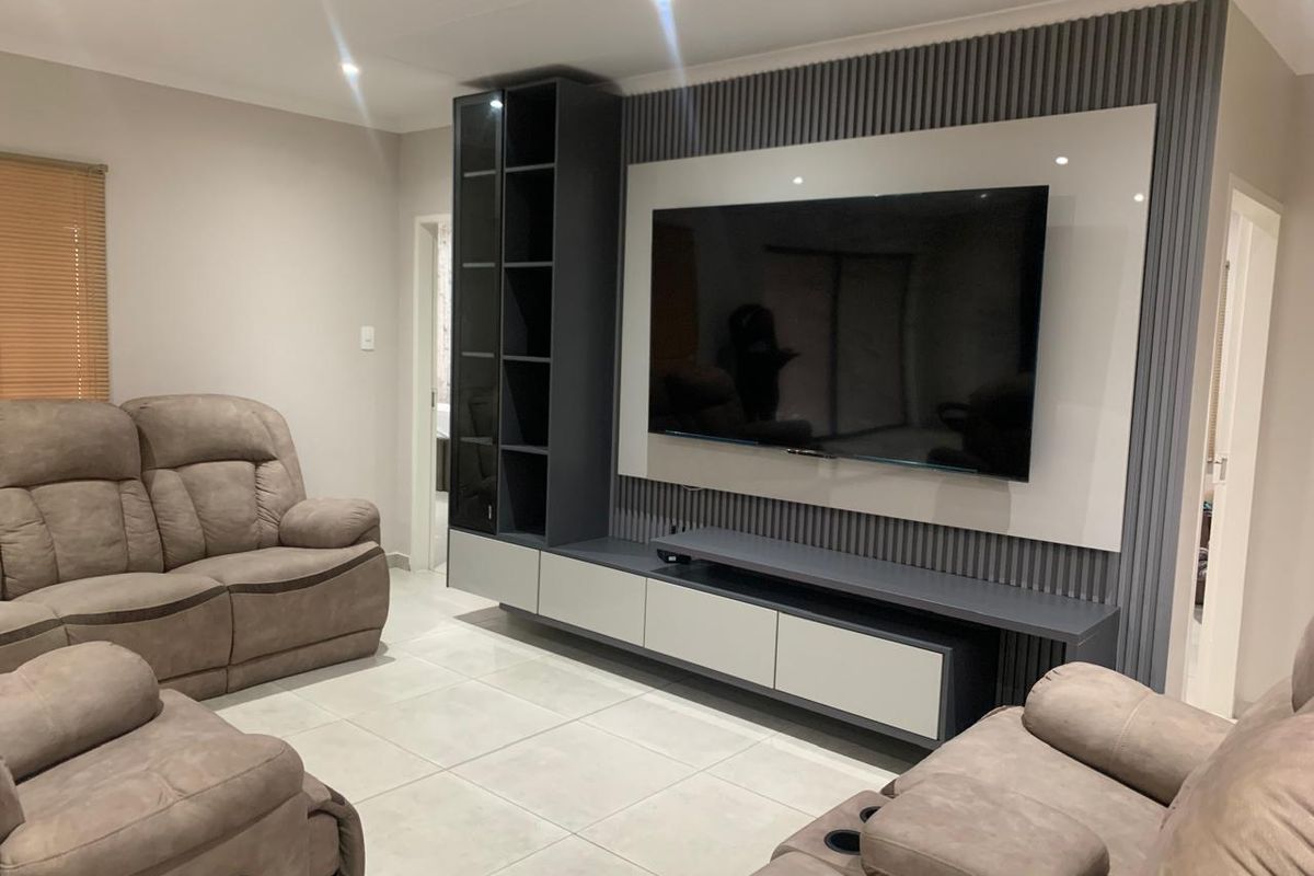 Modern living room featuring a custom built-in media wall unit with integrated shelving, slatted feature paneling, and neutral tiled flooring.