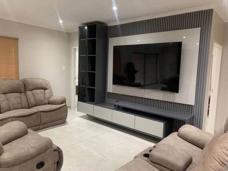 Modern living room featuring a custom built-in media wall unit with integrated shelving, slatted feature paneling, and neutral tiled flooring.