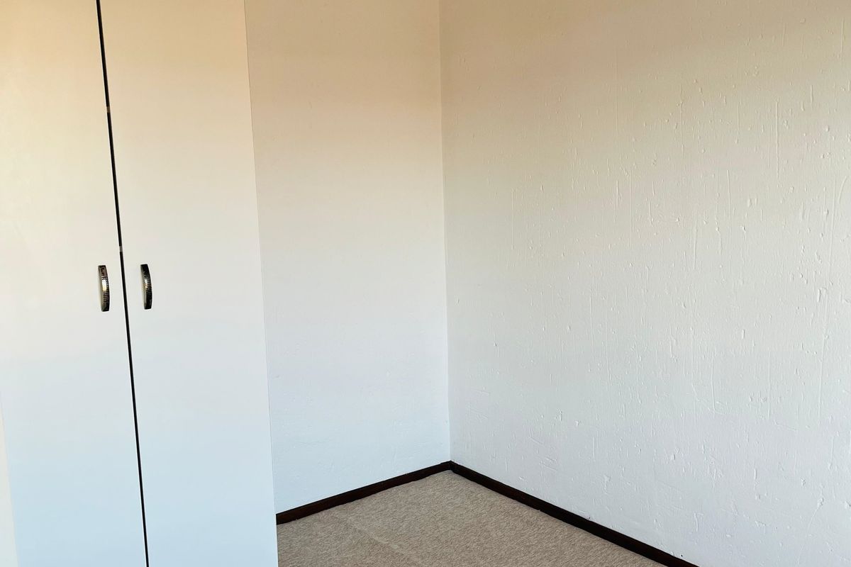 A clean, empty bedroom featuring neutral carpeting and a white built-in wardrobe, providing a blank canvas for personalization.