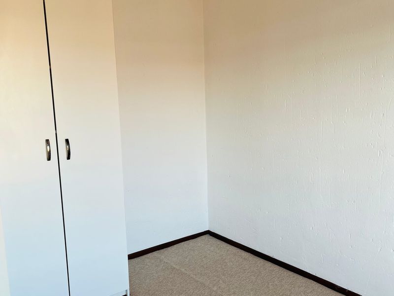 A clean, empty bedroom featuring neutral carpeting and a white built-in wardrobe, providing a blank canvas for personalization.