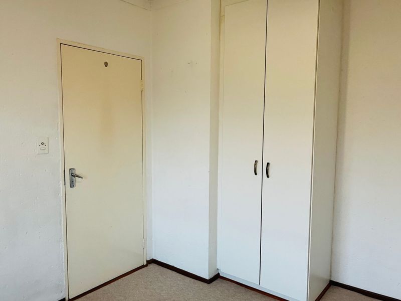 An empty bedroom featuring a built-in wardrobe, standard internal door, and carpet flooring, presenting a blank canvas for potential updates.