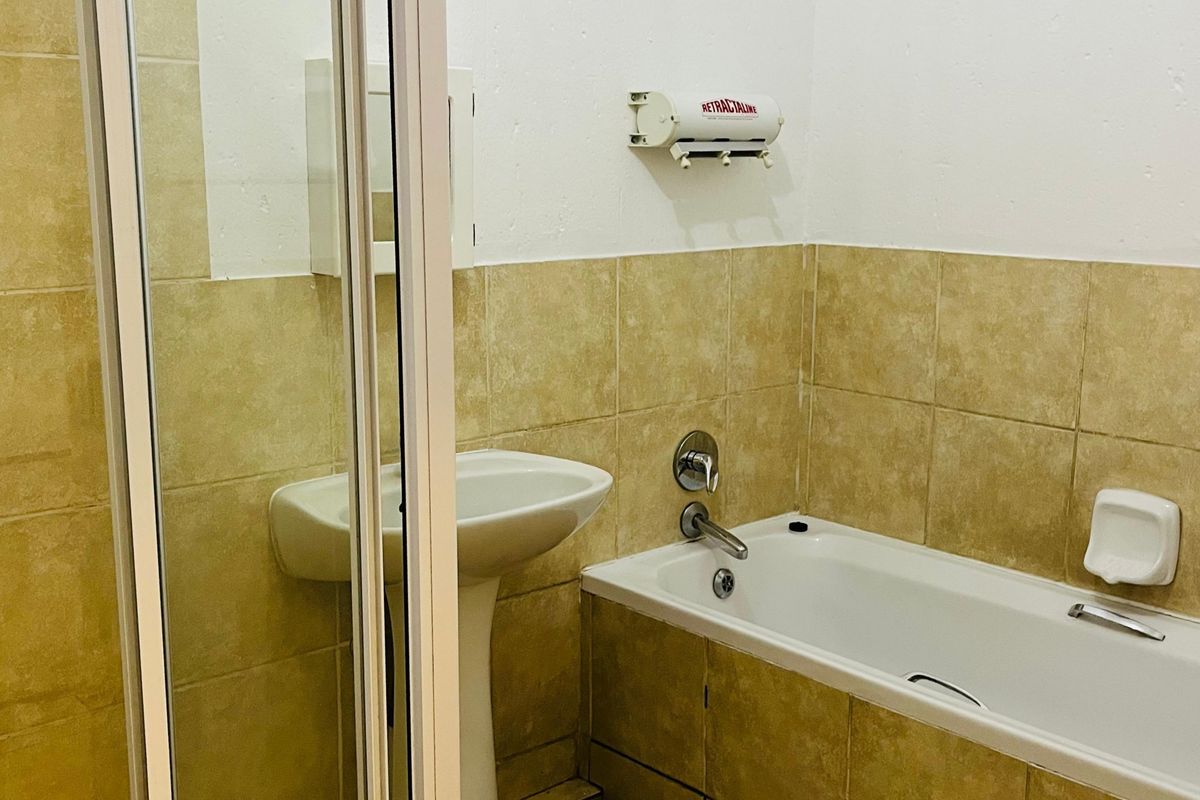 A functional bathroom featuring a pedestal basin, a bathtub with a shower enclosure, and neutral wall and floor tiling.