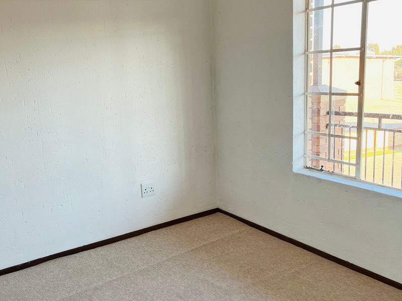 A vacant bedroom featuring neutral carpeting, white walls, and a window fitted with security burglar bars.