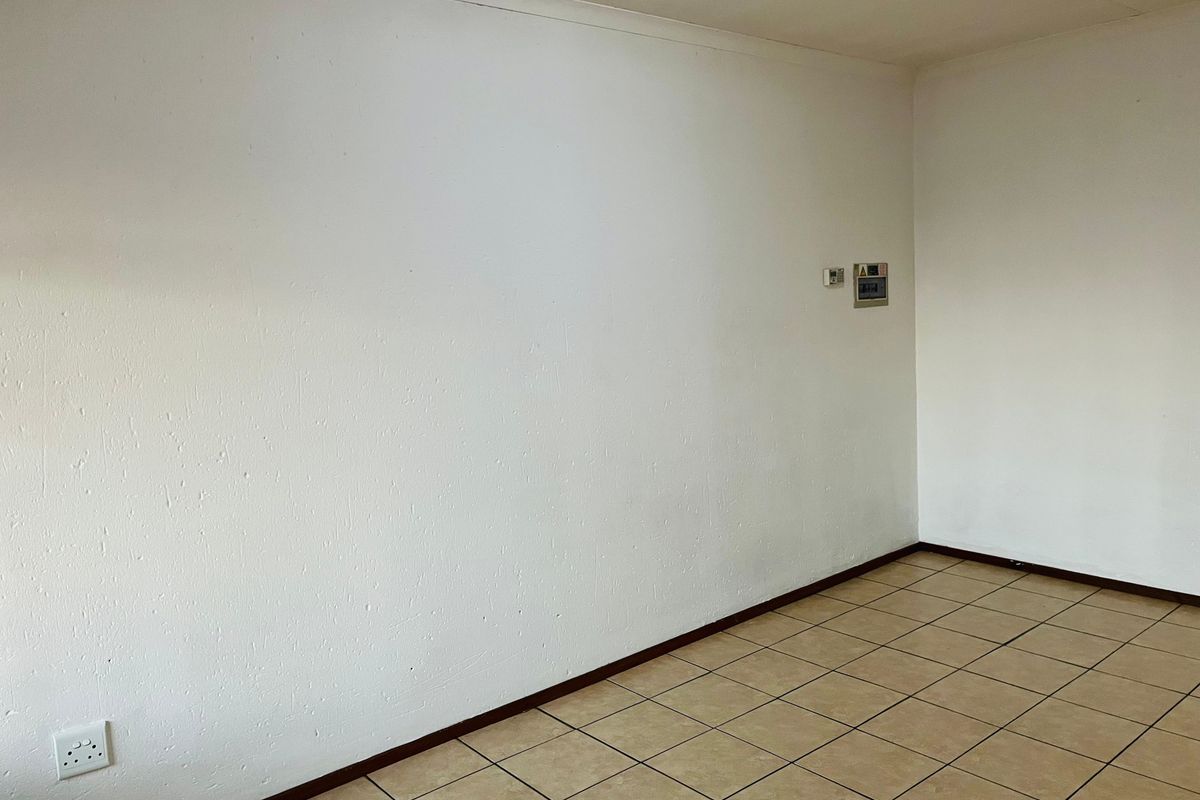 An empty living area featuring neutral ceramic floor tiles, white walls, and a wall-mounted electrical distribution board.