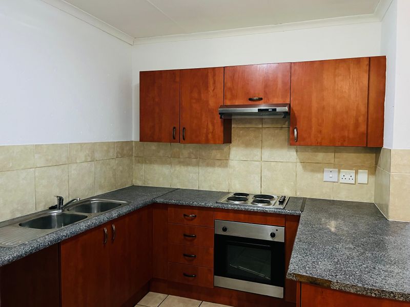A functional kitchen featuring wood-finish cabinetry, granite countertops, a built-in oven, hob, and extractor fan with neutral wall and floor tiling.