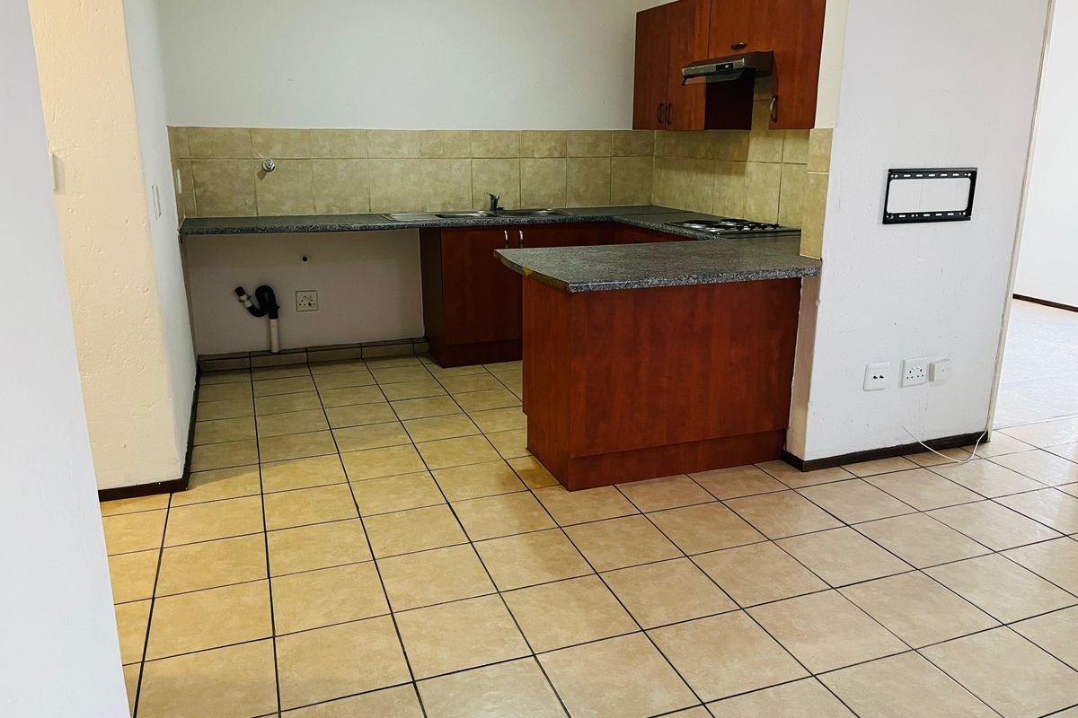 A functional kitchen featuring laminate cabinetry, granite countertops, a built-in hob with extractor fan, and tiled flooring, offering a clean, blank canvas for updates.