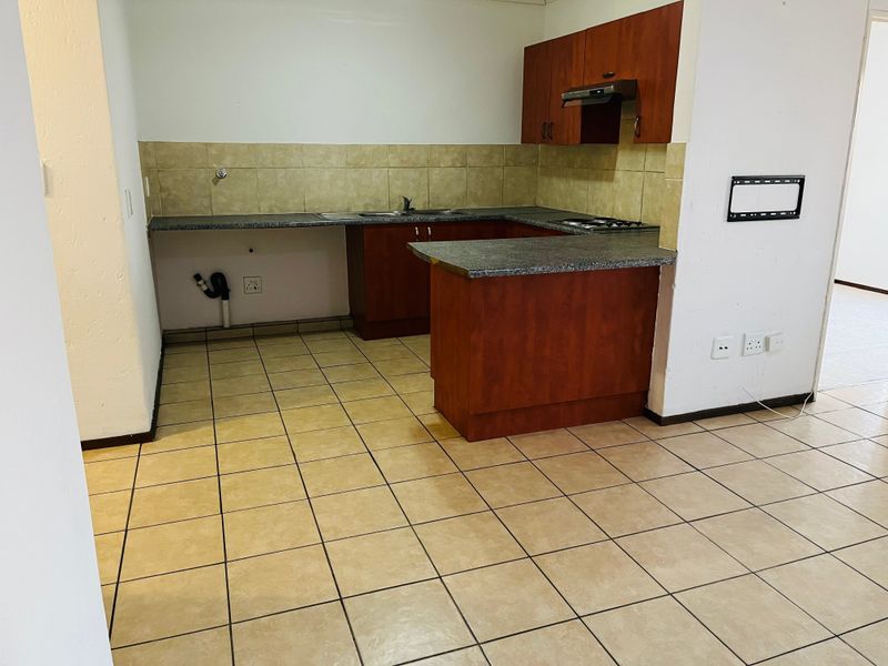 A functional kitchen featuring laminate cabinetry, granite countertops, a built-in hob with extractor fan, and tiled flooring, offering a clean, blank canvas for updates.