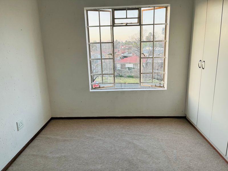 An empty bedroom featuring built-in cupboards, carpeted flooring, and a steel-framed window with views of the surrounding neighborhood.