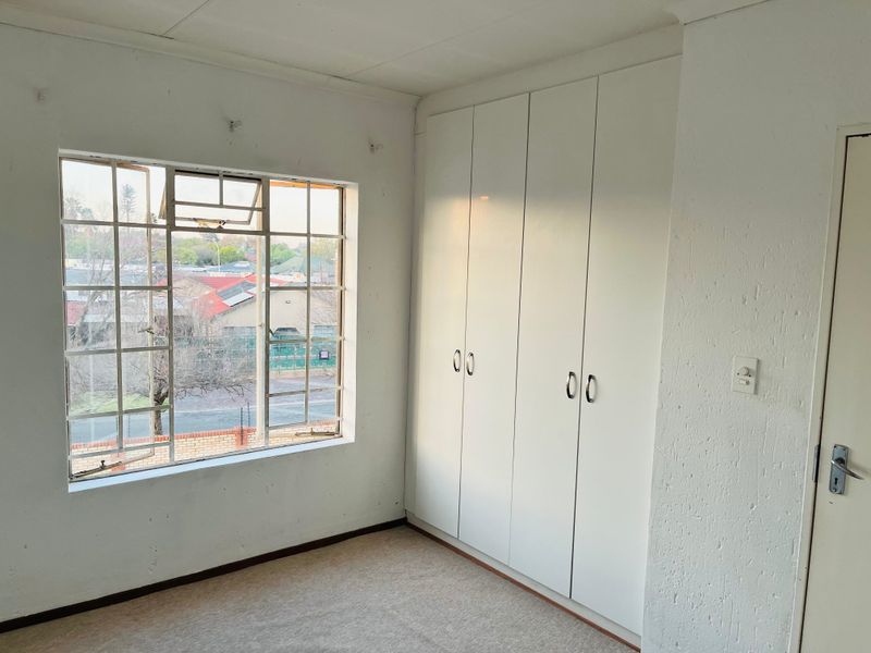 An empty bedroom featuring built-in cupboards, carpeted flooring, and a large steel-framed window with views of the surrounding neighborhood.