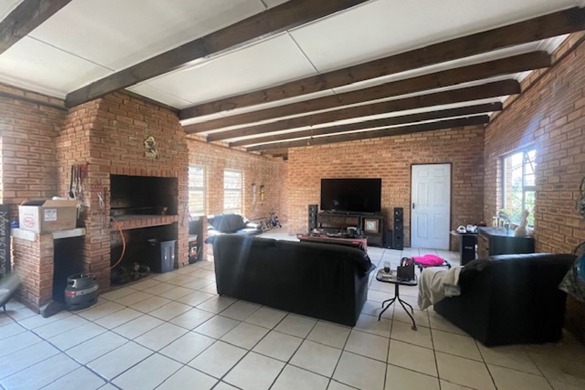 Spacious living room featuring exposed brick walls, timber ceiling beams, and a large built-in brick fireplace, finished with neutral floor tiles.