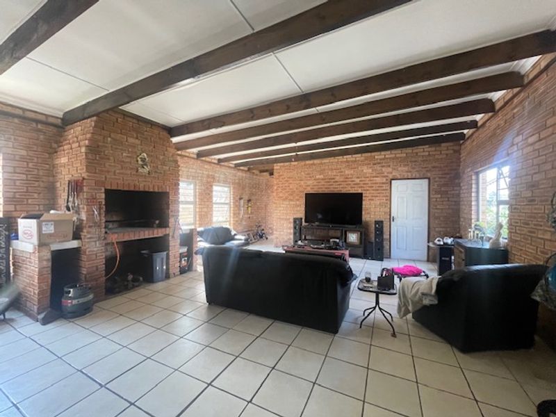 Spacious living room featuring exposed brick walls, timber ceiling beams, and a large built-in brick fireplace, finished with neutral floor tiles.
