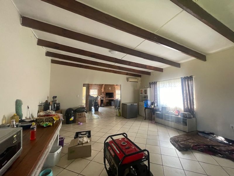 Spacious open-plan living area featuring exposed timber ceiling beams, ceramic tiled flooring, and a built-in brick fireplace in the adjacent room.