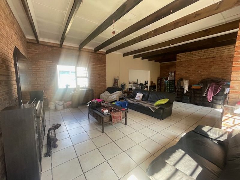 Spacious living area featuring exposed timber ceiling beams, rustic facebrick walls, and ceramic tiled flooring, offering a solid foundation for renovation.