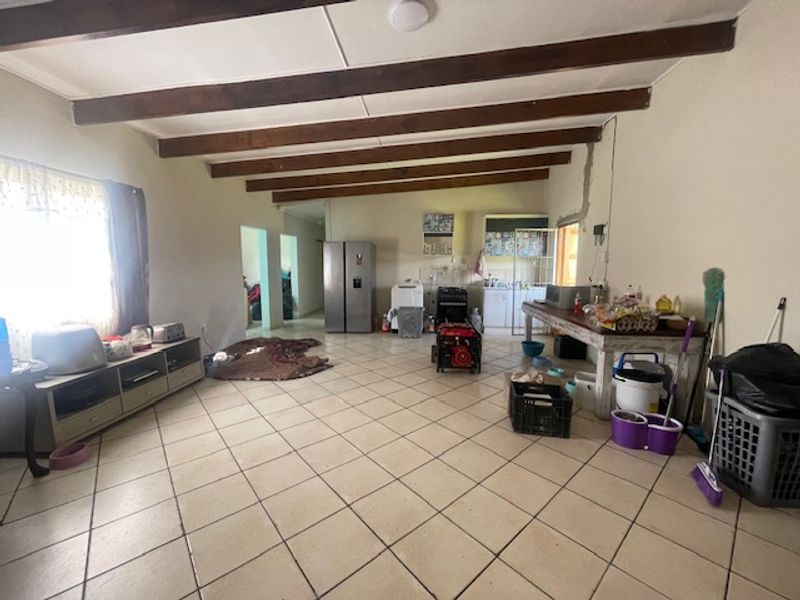 Spacious open-plan living and kitchen area featuring exposed timber ceiling beams and tiled flooring, requiring some cosmetic updates and electrical finishing.