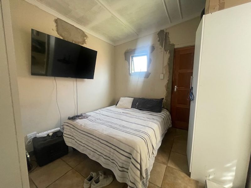 A compact bedroom featuring tiled flooring and a timber door, currently requiring wall repairs and cosmetic finishing to improve the overall aesthetic.