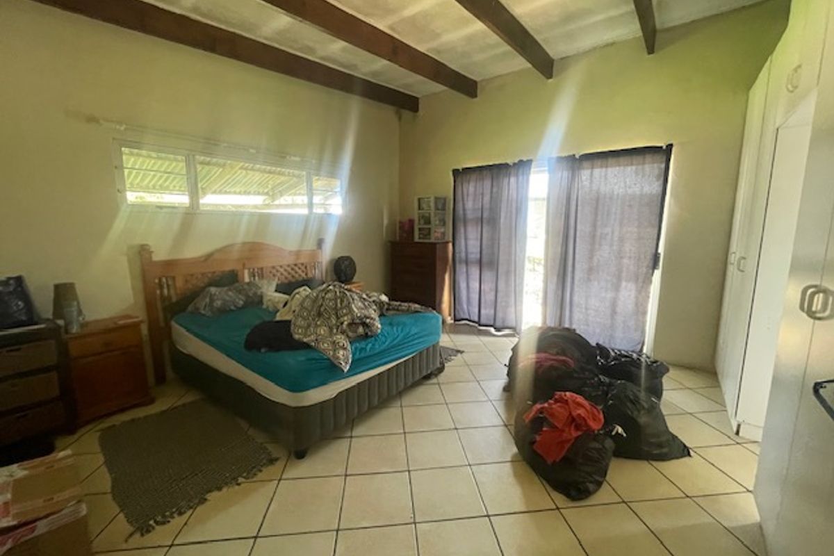 Spacious bedroom featuring exposed timber ceiling beams, tiled flooring, built-in cupboards, and direct access to the outdoors via a sliding glass door.