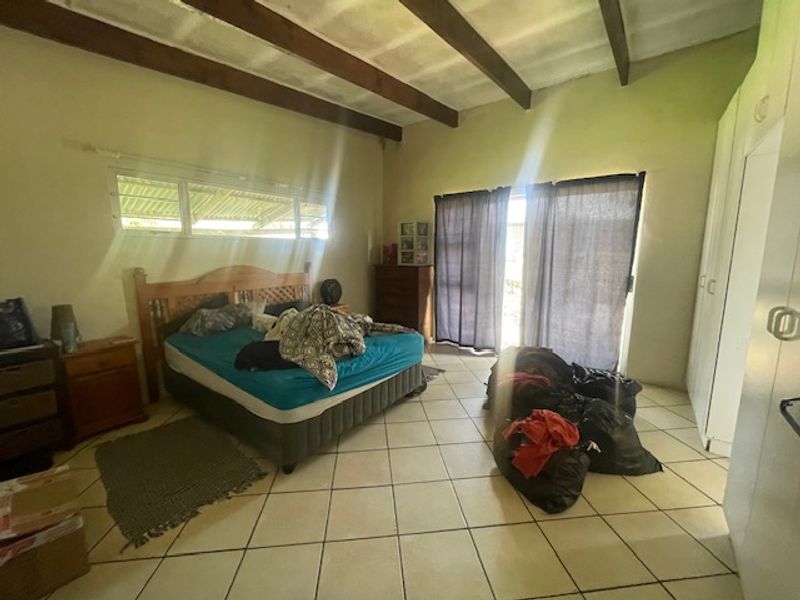 Spacious bedroom featuring exposed timber ceiling beams, tiled flooring, built-in cupboards, and direct access to the outdoors via a sliding glass door.