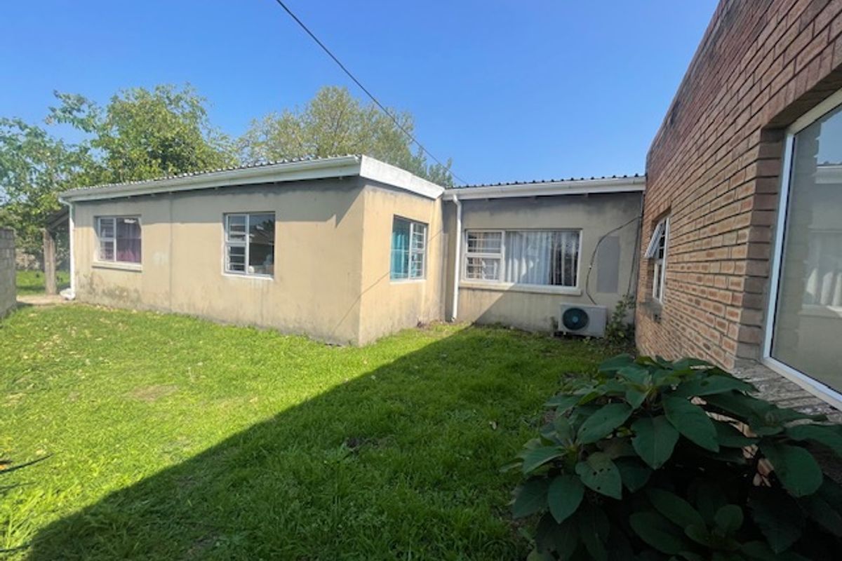 Rear view of the house showing a grassed garden area, brick and plastered exterior walls, and installed air conditioning unit.