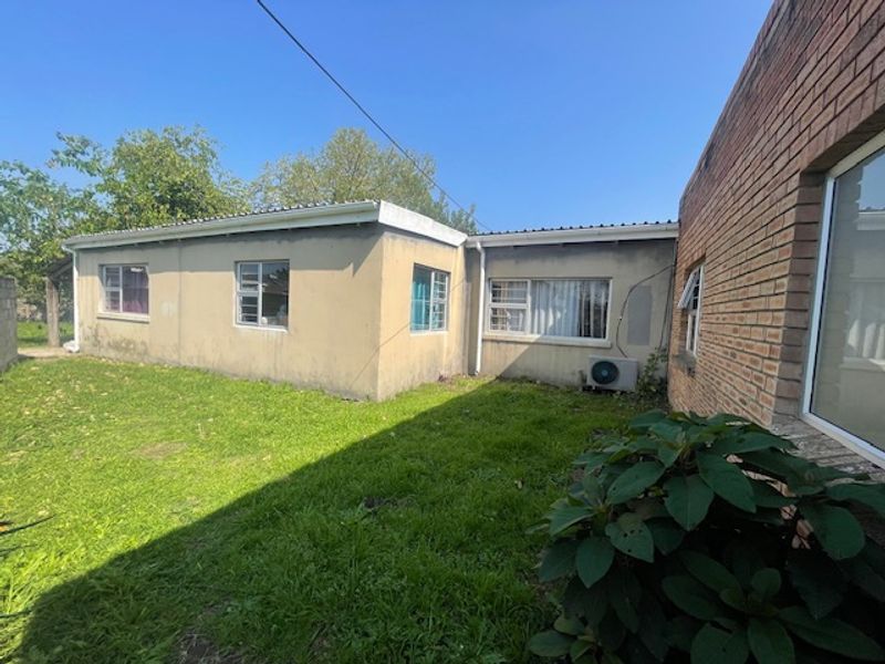 Rear view of the house showing a grassed garden area, brick and plastered exterior walls, and installed air conditioning unit.