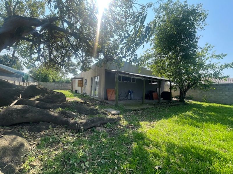 Rear view of the property featuring a covered patio area, sliding glass doors, and a spacious garden with mature trees and perimeter walling.