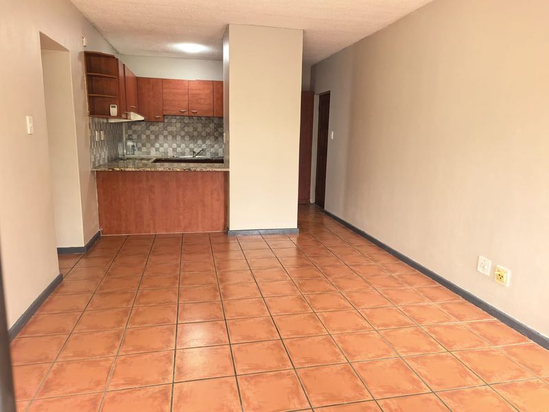 An open-plan living and kitchen area featuring tiled flooring, built-in wooden cabinetry, granite countertops, and a tiled backsplash.