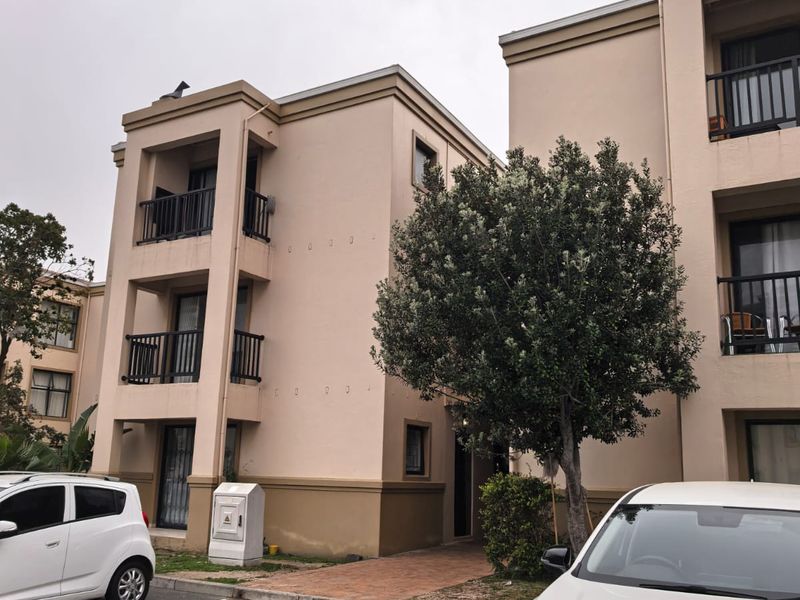 Exterior view of a multi-story apartment complex featuring balconies, paved walkways, and dedicated parking bays.
