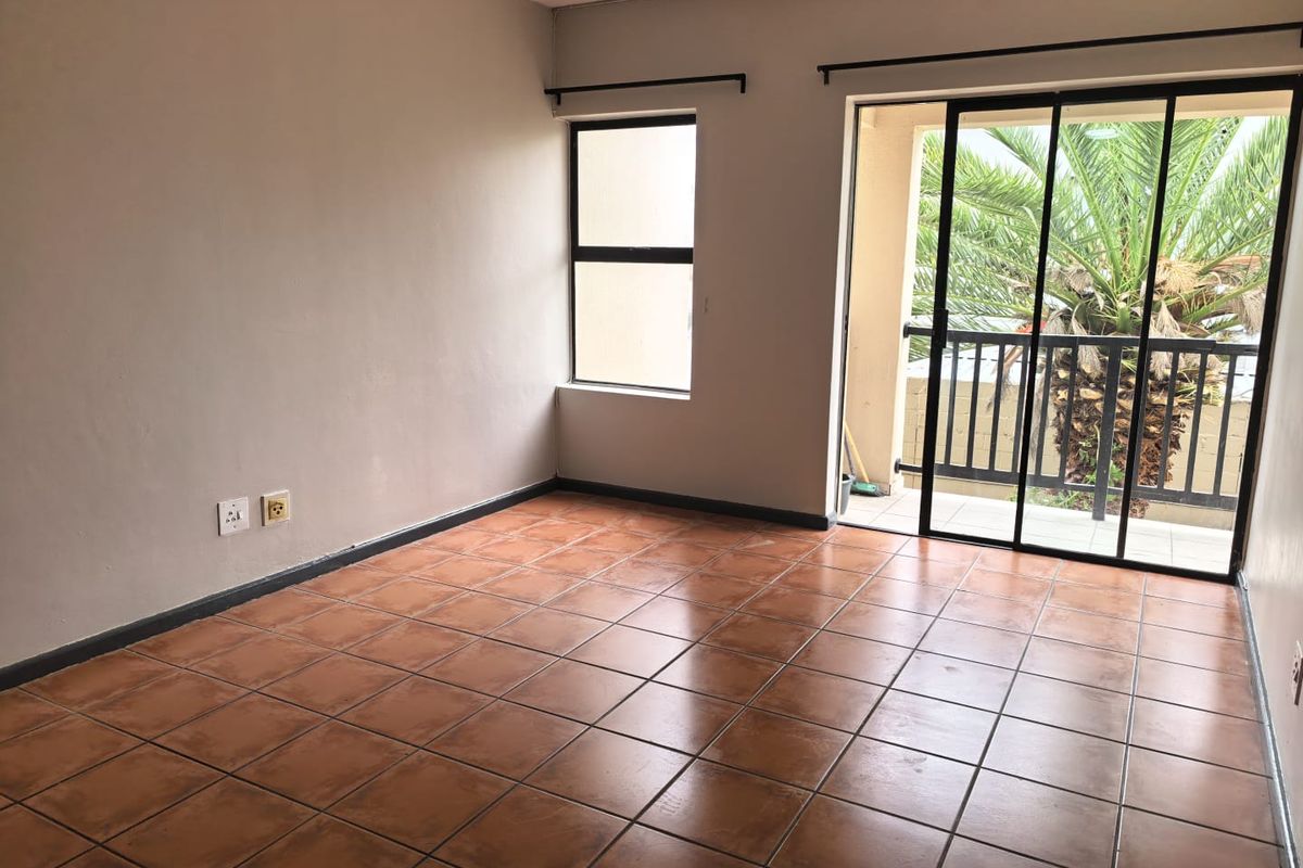An empty living room featuring terracotta floor tiles, neutral walls, and a sliding glass door providing access to a balcony.