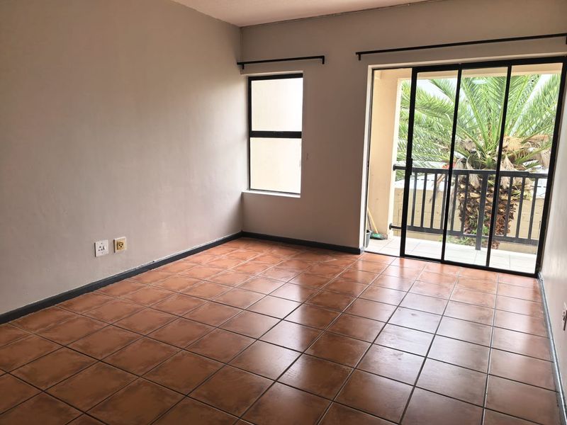 An empty living room featuring terracotta floor tiles, neutral walls, and a sliding glass door providing access to a balcony.