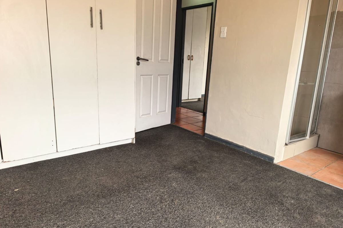 An empty bedroom featuring built-in cupboards, carpeted flooring, and direct access to an adjoining bathroom area with a shower enclosure.