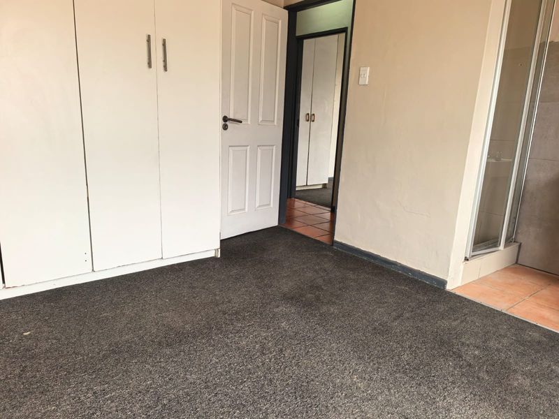 An empty bedroom featuring built-in cupboards, carpeted flooring, and direct access to an adjoining bathroom area with a shower enclosure.