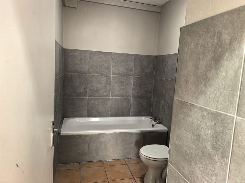A functional bathroom featuring a bathtub, toilet, and grey tiled wall finishes with contrasting floor tiles.