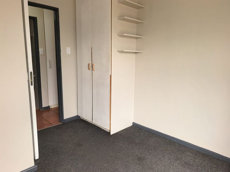 An empty bedroom featuring built-in wardrobe storage, wall-mounted shelving, and carpet flooring, providing a blank canvas for potential updates.
